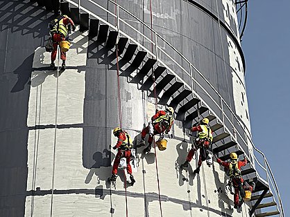Three rope-access technicians on curved silo façade